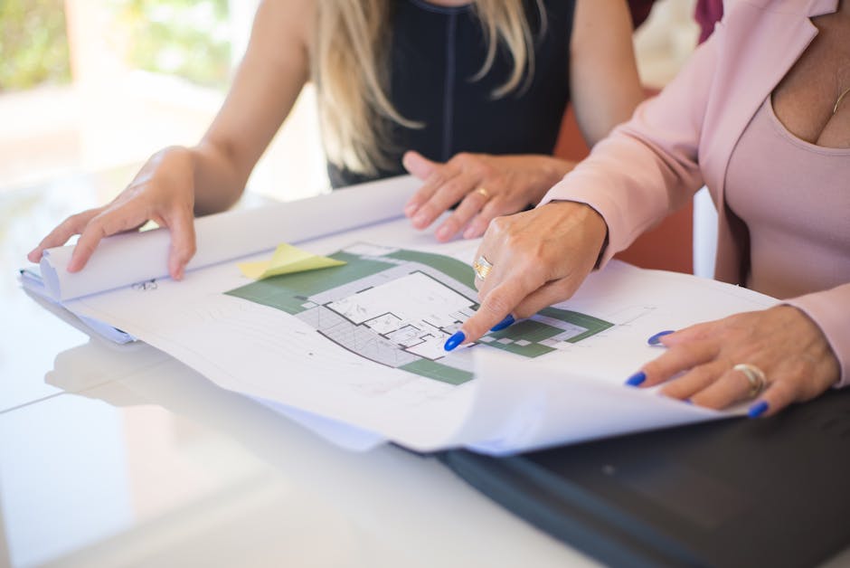 Two women reviewing detailed architectural blueprints in a professional setting.