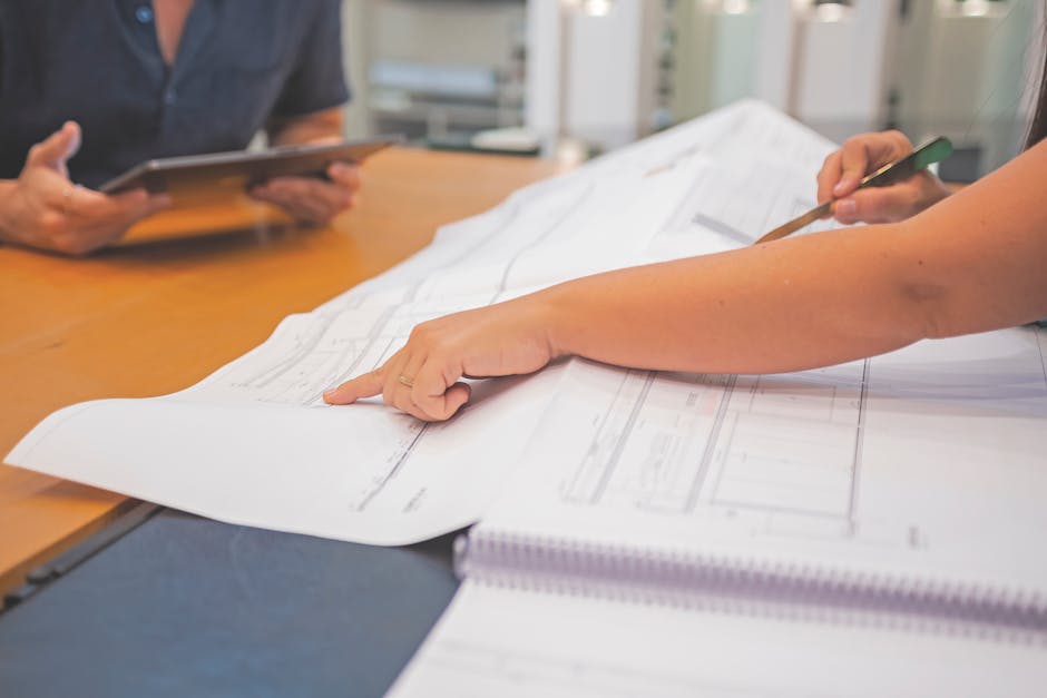 Two individuals collaborating on blueprints in a modern office setting, emphasizing teamwork.